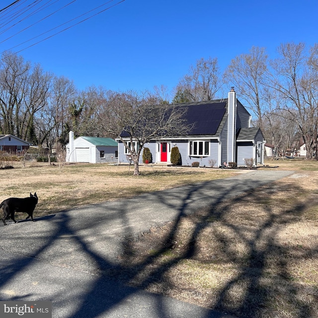 view of front of house featuring driveway, solar panels, a chimney, an outdoor structure, and a front yard