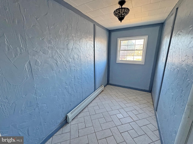 spare room with a baseboard heating unit, a textured wall, and baseboards