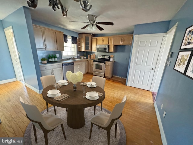 kitchen with stainless steel appliances, light wood-type flooring, a sink, and baseboards