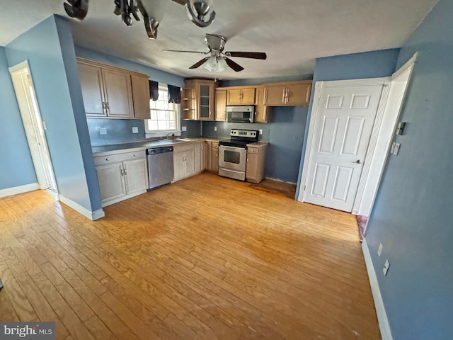 kitchen with light wood-style flooring, appliances with stainless steel finishes, a ceiling fan, a sink, and baseboards