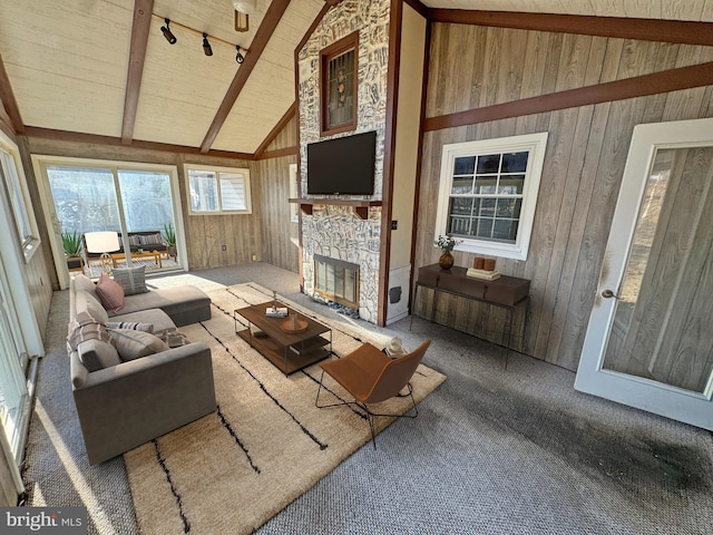 living area with carpet, rail lighting, wood walls, a stone fireplace, and beamed ceiling