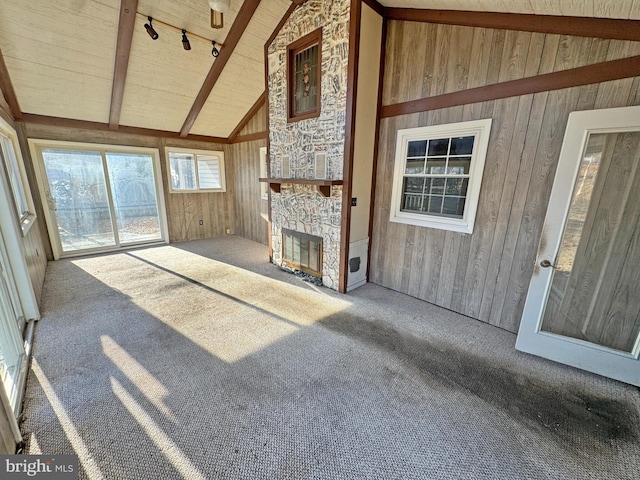 unfurnished living room featuring rail lighting, carpet floors, wood walls, a fireplace, and beam ceiling