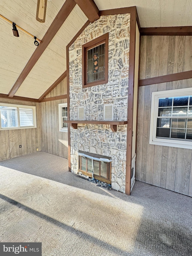 unfurnished living room with lofted ceiling with beams, carpet flooring, wood walls, a stone fireplace, and wooden ceiling