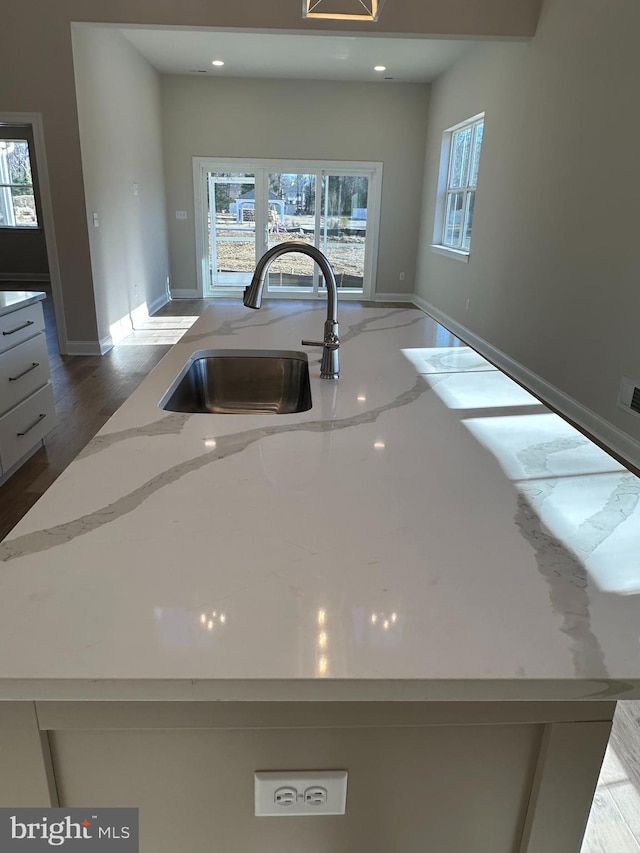 room details featuring recessed lighting, a sink, baseboards, light stone countertops, and an island with sink