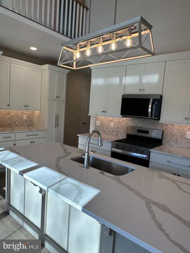 kitchen featuring decorative backsplash, decorative light fixtures, stainless steel appliances, white cabinetry, and a sink