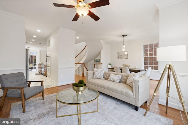 living room featuring light wood-type flooring, crown molding, and stairway