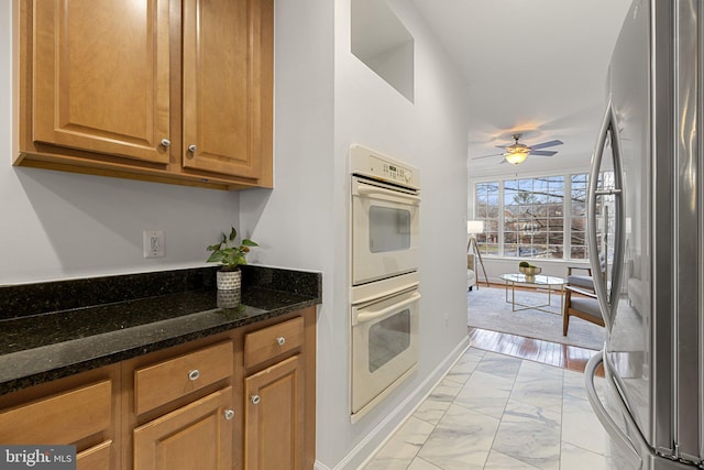 kitchen featuring dark stone counters, ceiling fan, freestanding refrigerator, marble finish floor, and double oven