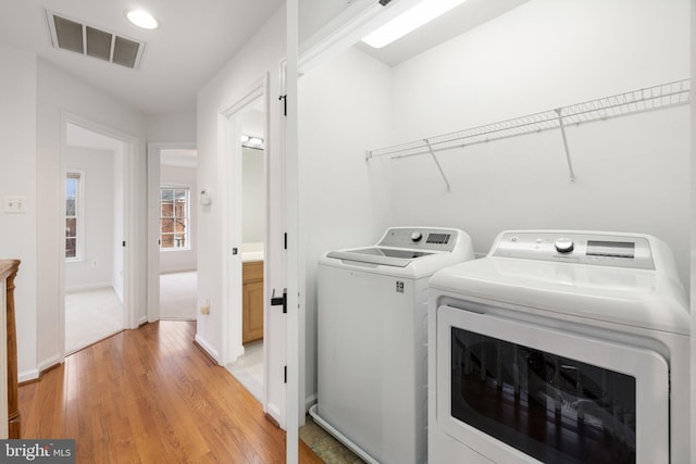 clothes washing area with laundry area, visible vents, baseboards, washer and dryer, and light wood-type flooring