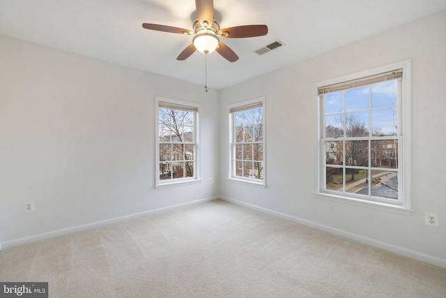 carpeted spare room featuring ceiling fan, visible vents, and baseboards