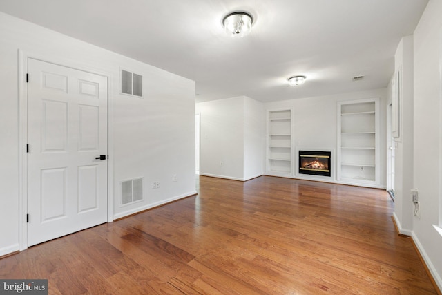 unfurnished living room with built in features, a glass covered fireplace, visible vents, and wood finished floors