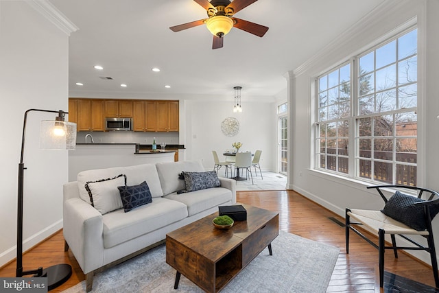 living area featuring baseboards, a ceiling fan, ornamental molding, light wood-style floors, and recessed lighting