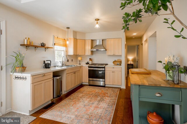 kitchen with a sink, wooden counters, stainless steel range with gas cooktop, wall chimney range hood, and dark wood-style flooring