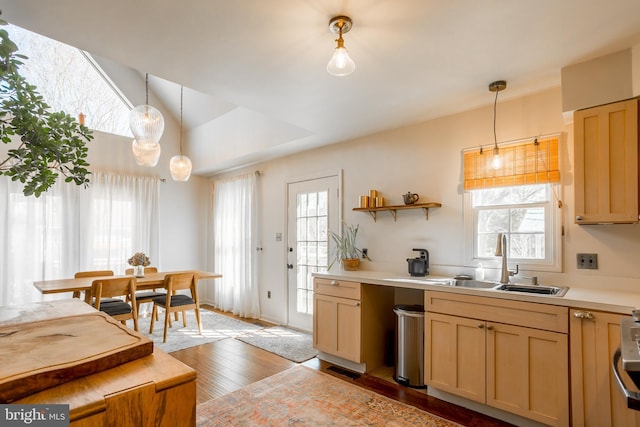 kitchen with light brown cabinets, a sink, decorative light fixtures, wood finished floors, and light countertops