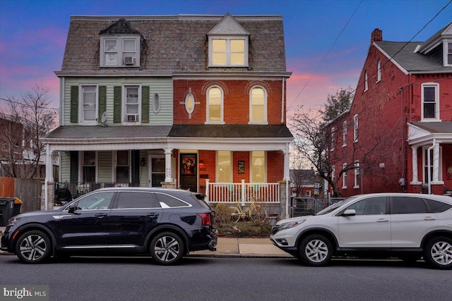 view of front of property with covered porch, brick siding, and mansard roof