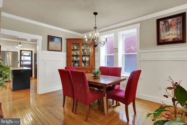 dining room with light wood finished floors, wainscoting, crown molding, a chandelier, and a decorative wall