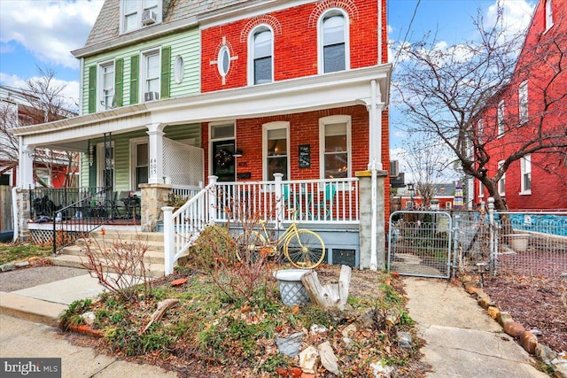 view of front of home with brick siding, mansard roof, a porch, a gate, and fence