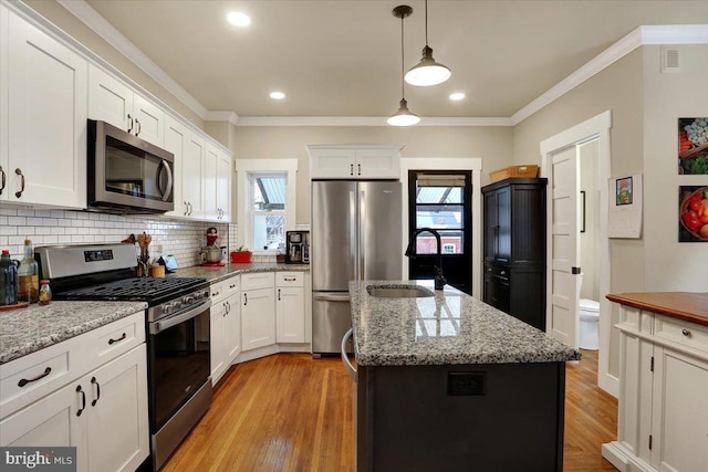 kitchen with stainless steel appliances, a kitchen island with sink, ornamental molding, and backsplash