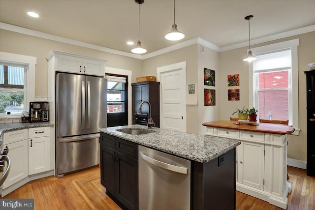 kitchen featuring appliances with stainless steel finishes, ornamental molding, white cabinets, a sink, and an island with sink