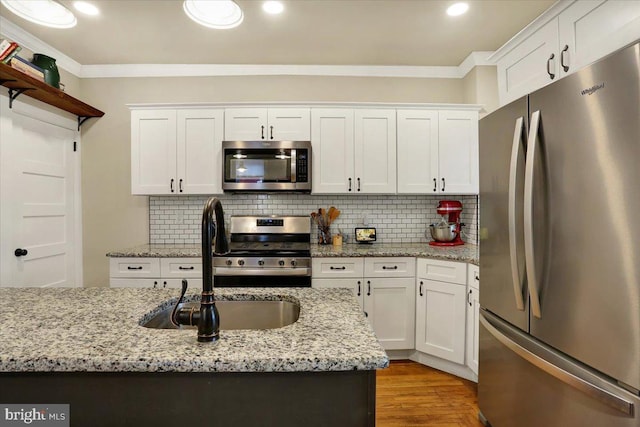 kitchen with tasteful backsplash, appliances with stainless steel finishes, crown molding, white cabinetry, and a sink