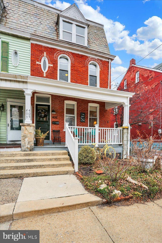 view of front of house featuring a high end roof, covered porch, brick siding, and mansard roof