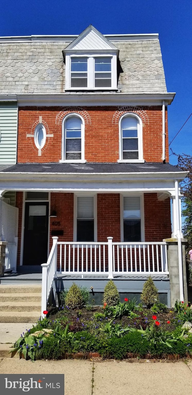 view of front of home featuring brick siding, mansard roof, and a porch