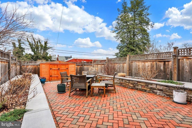 view of patio with an outbuilding, outdoor dining area, a fenced backyard, and a storage unit