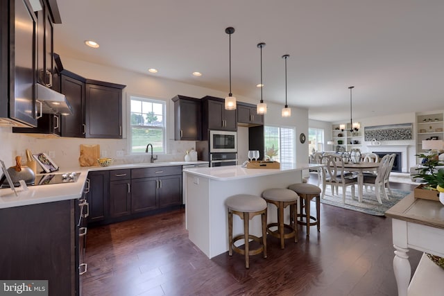 kitchen featuring dark wood-style floors, light countertops, appliances with stainless steel finishes, under cabinet range hood, and a kitchen breakfast bar