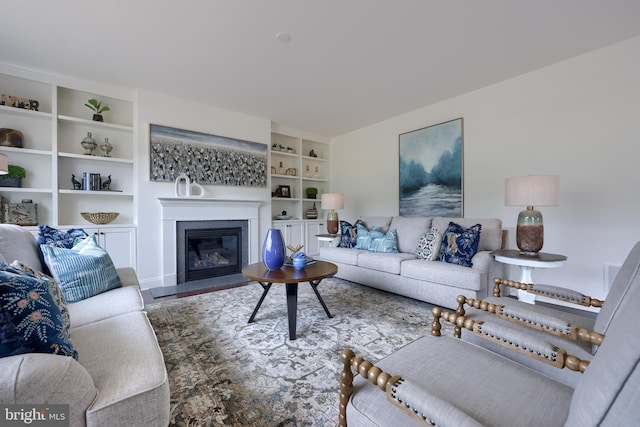 living area with a fireplace with flush hearth, built in shelves, and wood finished floors