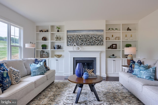 living area with dark wood-style floors, a glass covered fireplace, and built in shelves