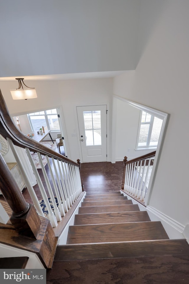 staircase featuring a towering ceiling, baseboards, and wood finished floors