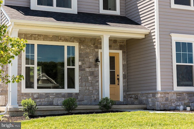 entrance to property featuring a shingled roof, stone siding, and a porch