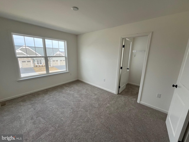 unfurnished bedroom with carpet flooring, visible vents, baseboards, a closet, and a walk in closet