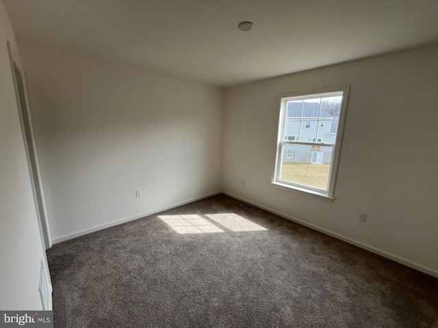 empty room featuring dark colored carpet, visible vents, and baseboards