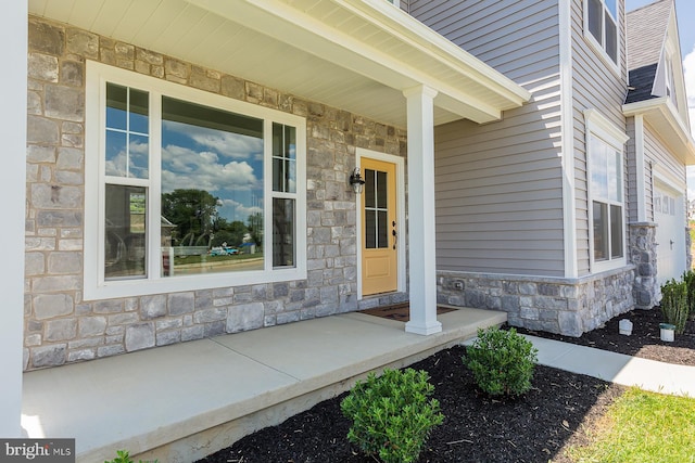 property entrance featuring stone siding, a porch, and a shingled roof