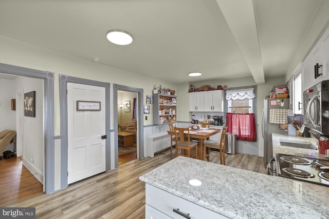 kitchen with white cabinets, radiator heating unit, light wood-style flooring, light stone countertops, and stainless steel appliances