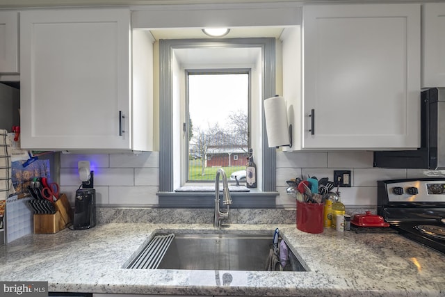 kitchen with tasteful backsplash, white cabinetry, light stone counters, and a sink