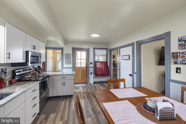 kitchen with light stone counters, white cabinetry, stainless steel appliances, and wood finished floors