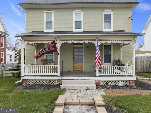 view of front of home with brick siding, roof with shingles, covered porch, fence, and a front yard