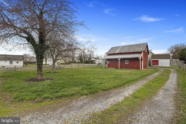 view of home's exterior with a barn, driveway, an outbuilding, fence, and a yard