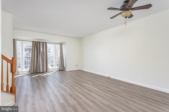 unfurnished room with baseboards, a ceiling fan, wood finished floors, and stairs