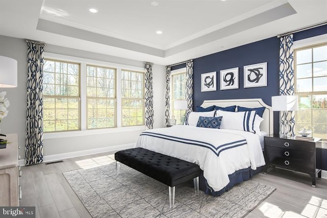 bedroom featuring wood finished floors, visible vents, baseboards, a tray ceiling, and crown molding