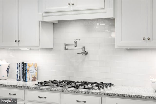 kitchen with tasteful backsplash, white cabinets, stainless steel gas stovetop, and light stone counters