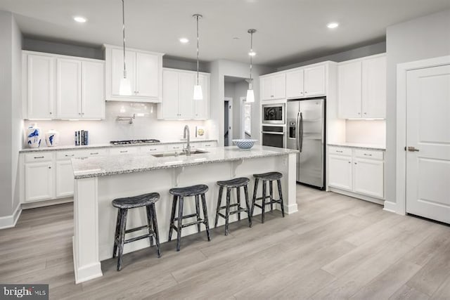 kitchen with light wood finished floors, appliances with stainless steel finishes, a kitchen breakfast bar, white cabinetry, and a sink