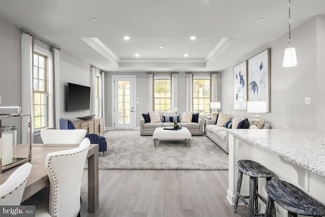 living area with ornamental molding, a raised ceiling, light wood-style flooring, and recessed lighting