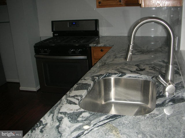 room details with stone counters, brown cabinets, tasteful backsplash, a sink, and gas range