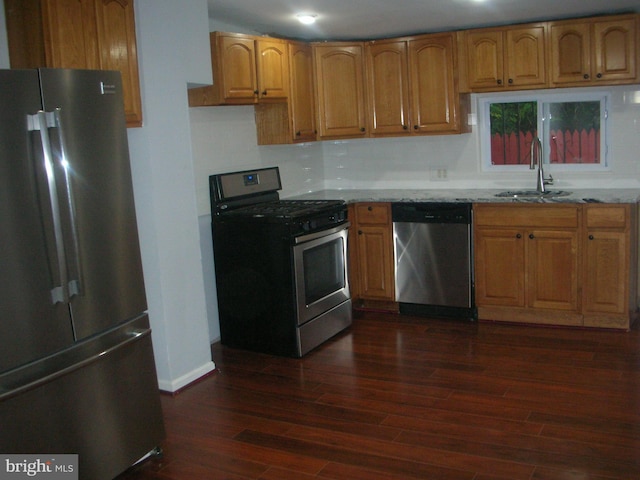 kitchen with stainless steel appliances, light stone countertops, a sink, and dark wood-style floors