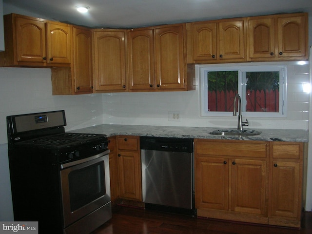 kitchen with light stone countertops, appliances with stainless steel finishes, brown cabinets, and a sink