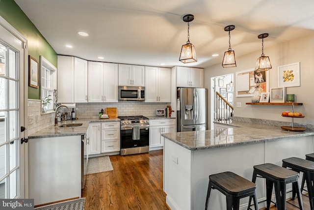 kitchen featuring a sink, backsplash, white cabinetry, stainless steel appliances, and a peninsula