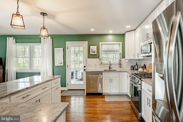 kitchen with dark wood-type flooring, a sink, stainless steel appliances, white cabinets, and decorative backsplash