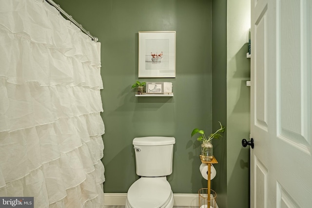 bathroom featuring curtained shower, baseboards, and toilet